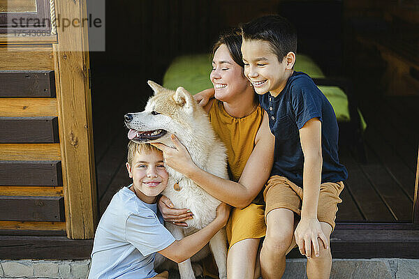 Glückliche Familie umarmt ihren Akita-Hund  der vor dem Haus sitzt