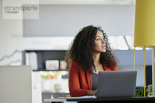 Nachdenkliche Geschäftsfrau mit Laptop am Schreibtisch im Büro