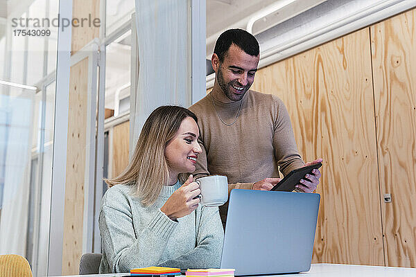 Geschäftsfrau hält Tasse mit Kollege in der Hand und nutzt Tablet-PC im Studio