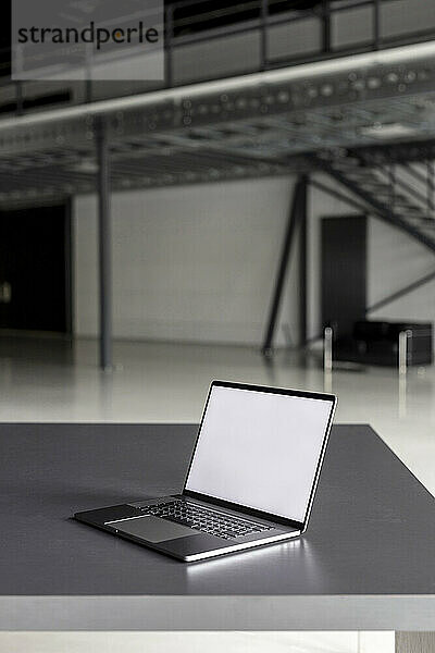 Laptop mit leerem Bildschirm auf dem Schreibtisch in der Industriehalle
