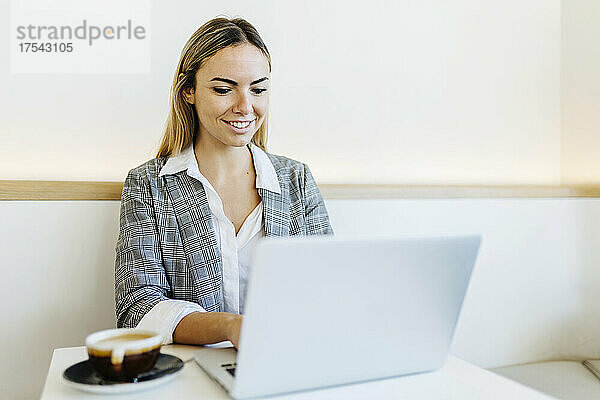 Smiling freelancer working on laptop in cafe