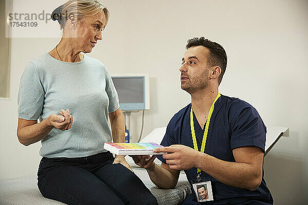 Krankenschwester hält Medikamentenbox und spricht mit Patient im Krankenzimmer