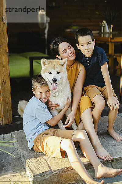 Mother and sons sitting at doorway with Akita dog