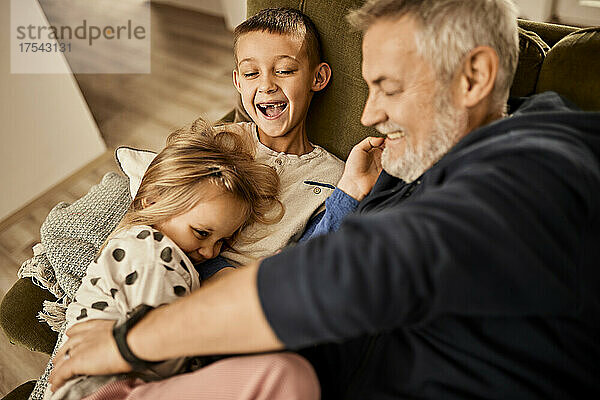 Cheerful grandfather playing with boy and girl at home