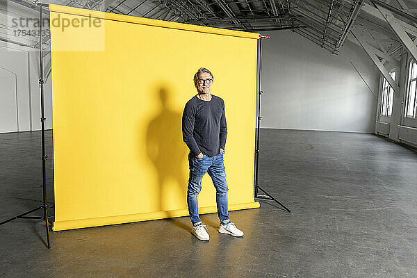 Businessman with hands in pockets at yellow backdrop