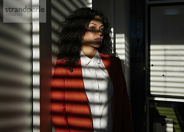 Sonnenlicht auf nachdenkliche Geschäftsfrau  die im Büro an der Wand lehnt
