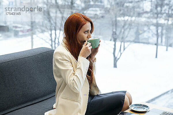 Berufstätige Frau trinkt Kaffee auf dem Sofa in der Bürokantine