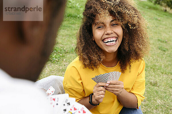 Frau lacht und spielt Karten mit Freund im Park