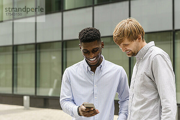 Smiling man sharing smart phone with friend