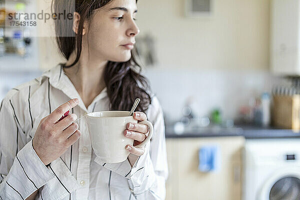 Junge Frau hält Teetasse in der heimischen Küche