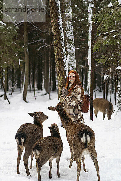 Frau steht neben Hirsch im Winterwald
