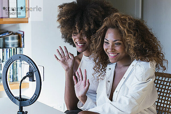Smiling friends waving hand at mobile phone attached to ring light