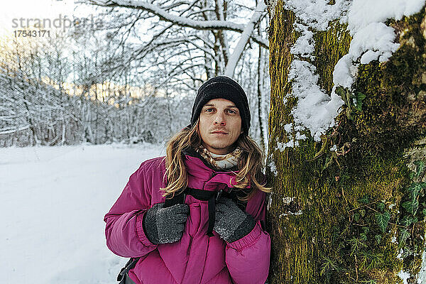 Tourist stützt sich auf Baumstamm im Winterwald