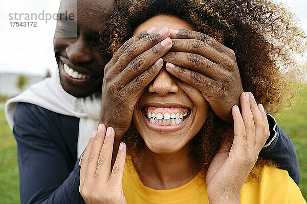 Happy young man covering friend's eyes with hands at park