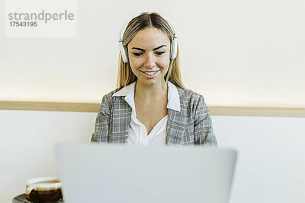 Businesswoman wearing headphones working on laptop in cafe
