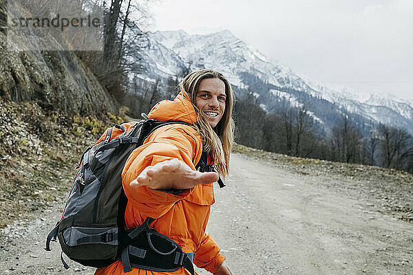 Fröhlicher Mann in orangefarbener Jacke  der auf einer Bergstraße läuft