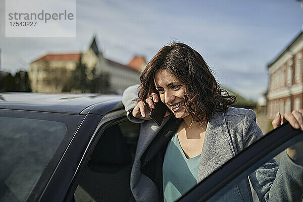 Smiling woman talking on mobile phone at car door