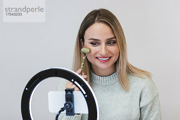Smiling influencer filming tutorial with jade roller in front of ring light