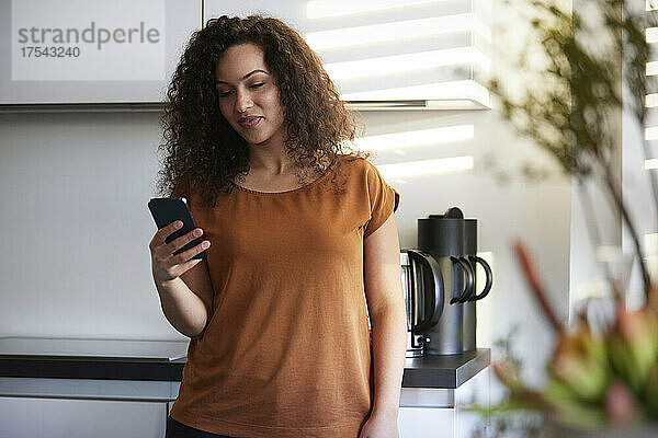 Lächelnde Geschäftsfrau benutzt Smartphone in Büroküche