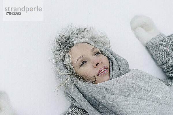 Nachdenkliche Frau mit grauem Schal  die auf Schnee liegt