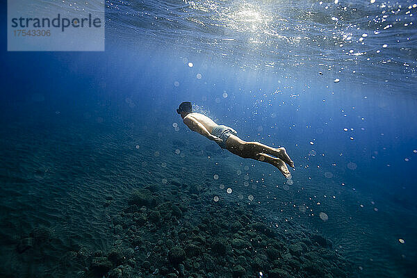 Nackter Oberkörper junger Mann schwimmt unter Wasser