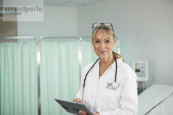 Lächelnder Arzt hält Tablet-PC im Arztzimmer