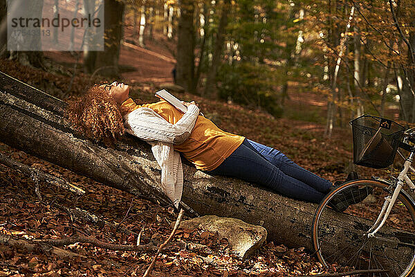 Carefree woman relaxing on log by bicycle in autumn forest