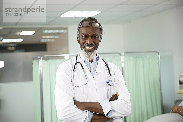 Confident male doctor with arms crossed in medical room