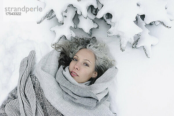 Woman in gray warm clothing lying on snow in winter