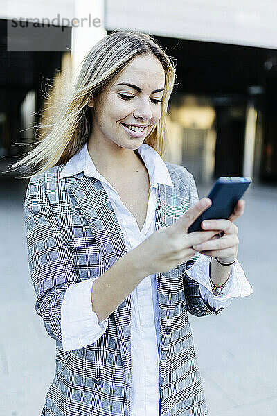 Lächelnde Geschäftsfrau mit blonden Haaren  die ihr Smartphone benutzt
