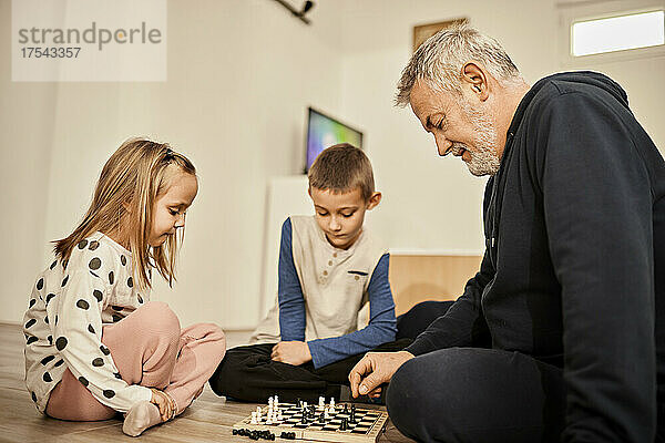 Boy and girl learning chess with grandfather at home