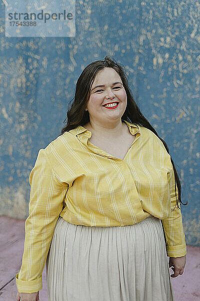 Smiling plus size woman standing in front of wall