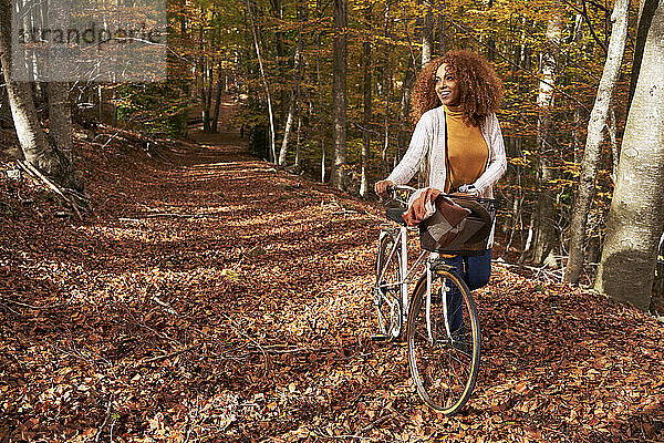 Woman wheeling bicycle on footpath in autumn forest