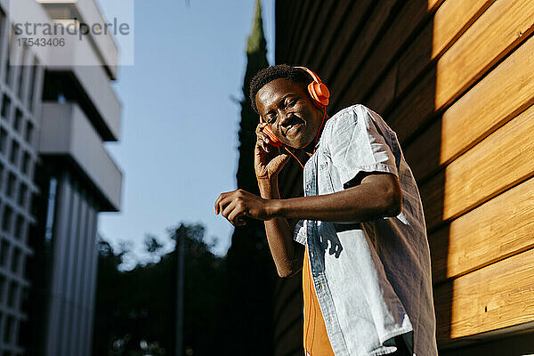 Smiling man enjoying music through headphones in city at sunset