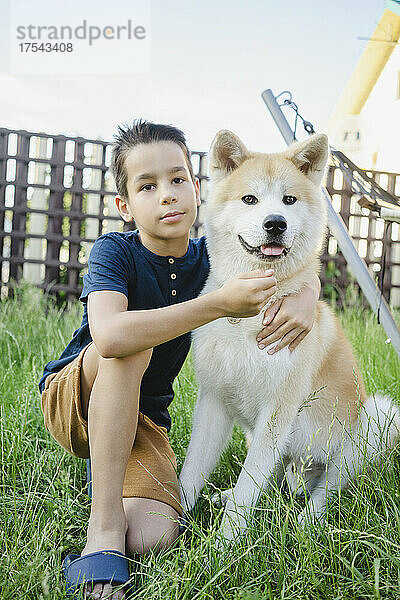 Netter Junge mit Akita-Hund  der auf Gras sitzt