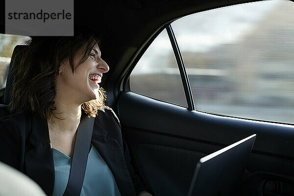 Happy businesswoman with laptop traveling in car