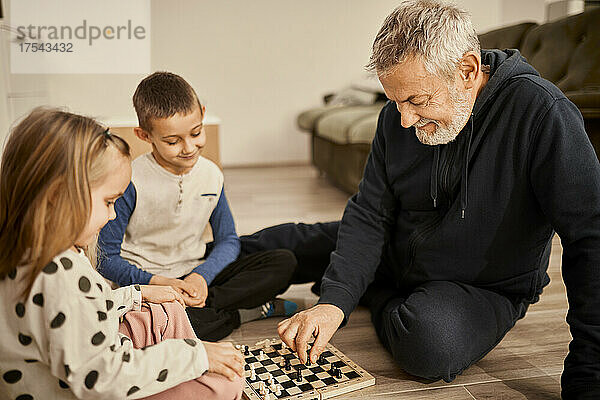 Grandfather teaching chess to grandchildren sitting at home
