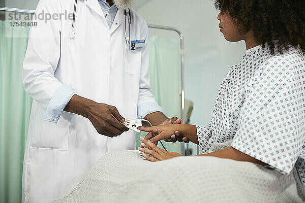 Doctor checking pulse of patient with oximeter at hospital