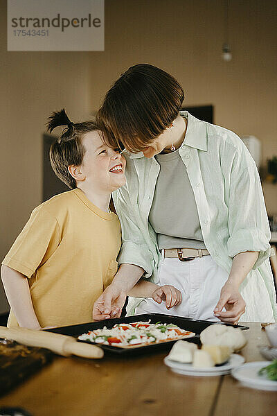 Happy son looking at mother preparing pizza together