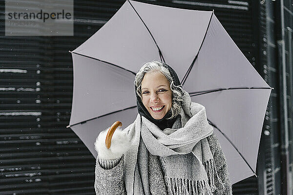 Happy woman wrapped in gray scarf holding umbrella