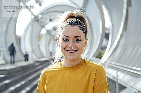 Smiling young woman at footbridge on sunny day