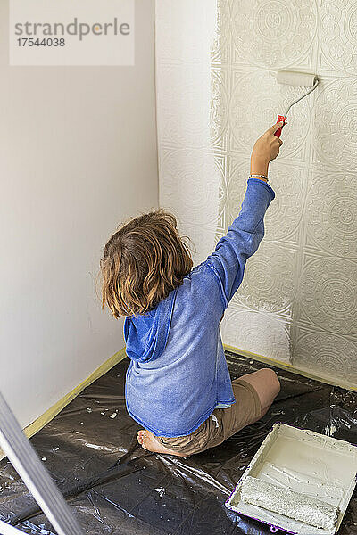 Achtjähriger Junge malt mit Farbroller eine Hauswand