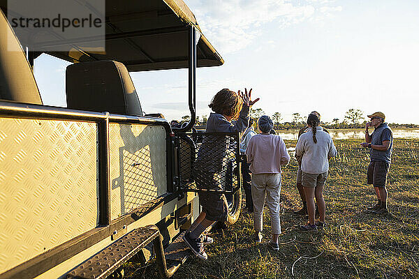 Menschen genießen einen Sundowner und Drinks bei Sonnenuntergang auf einer Safarifahrt.