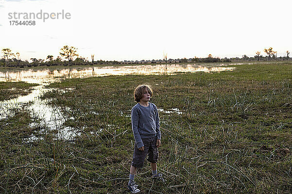 Ein Junge steht bei Sonnenuntergang allein in einer Deltalandschaft im Landesinneren.