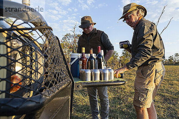 Menschen genießen einen Sundowner und Drinks bei Sonnenuntergang auf einer Safarifahrt.