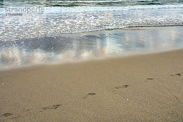 Fußspuren und Meereswelle am Sandstrand