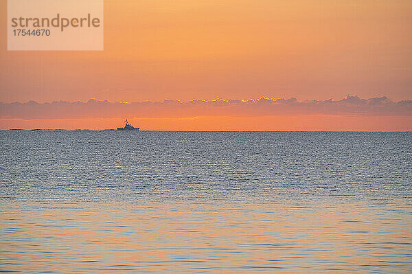 Ruhiges Meer bei Sonnenaufgang mit Fischerboot in der Ferne