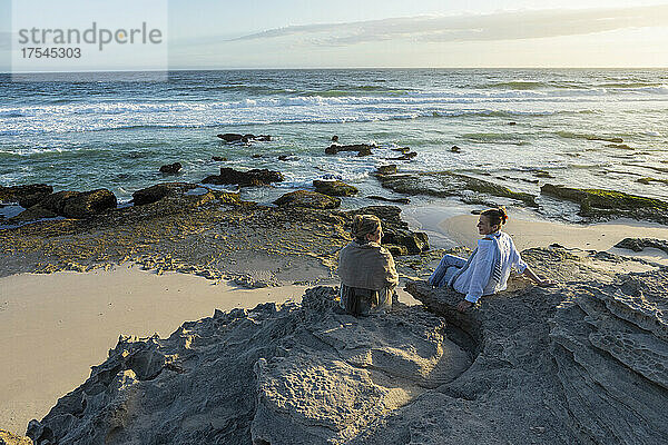 Südafrika  Westkap  Mutter und Tochter (16–17) sitzen bei Sonnenuntergang am Strand im Naturschutzgebiet Lekkerwater