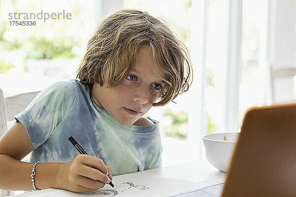 Junge (8-9) zeichnet während des Online-Unterrichts ein Bild
