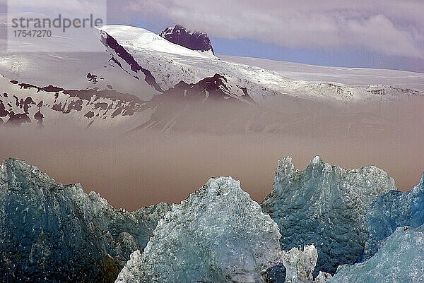 Blaues Eis spiegelt sich im Wasser  Berge ragen aus dem Nebel  Jökulsarlon  Gletscherlagune  Skandinavien  Island  Europa